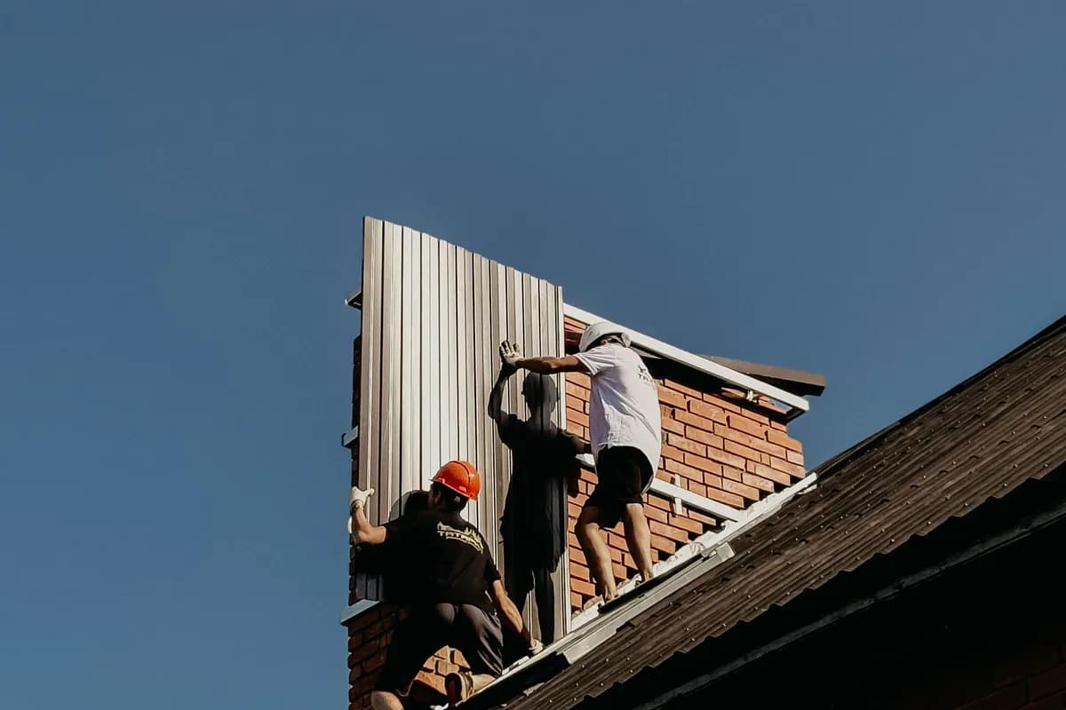 Workers installing metal roof panels on a brick house