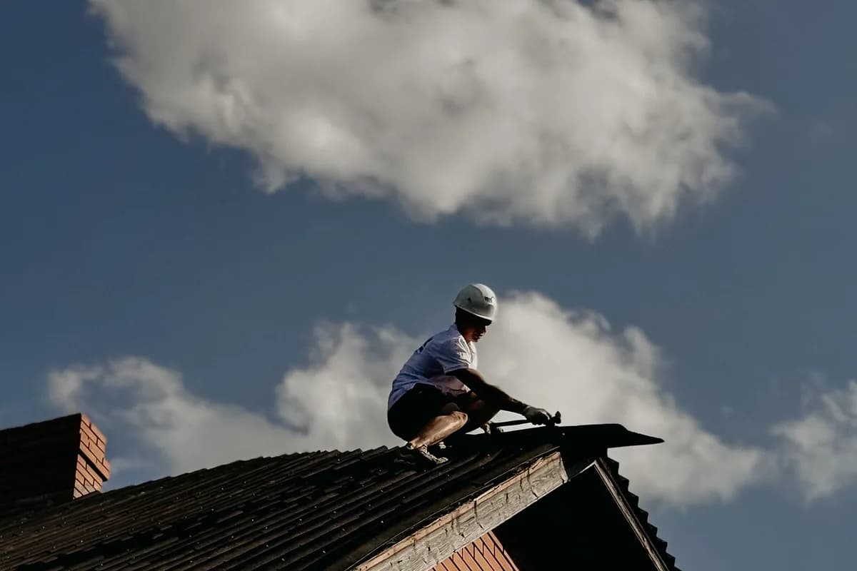 Contractor in protective gear repairing a roof on a sunny day